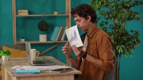 Medium Shot Capturing a Man Having a Videocall on a Laptop in His Home Office Discussing Graphs and