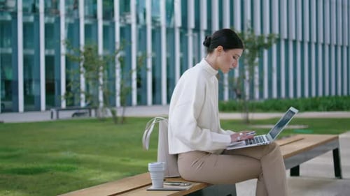 Woman Works on Laptop on Bench Near Office
