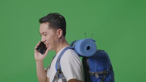 Close Up Side View Of Asian Male Hiker Talking On Smartphone While Walking On Green Screen