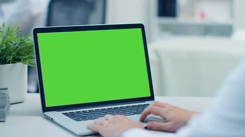 Close-up Shot of a Doctor Working on a Laptop with Green Screen On. His Colleague in the Background