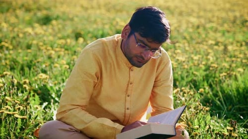 Young Indian Man Reading a Book in a Field of Flowers