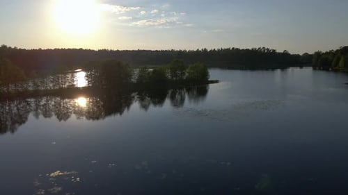 Calm lake landscape with trees reflecting in water at sunset as drone glides to the right.