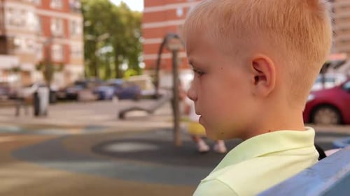 Closeup of a Sad Little Boy Sitting Alone on a Bench on the Playground