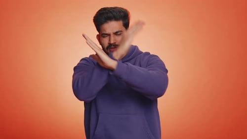 Un bel homme bouleversé en sweat à capuche montrant les pouces vers le bas, signe, geste, désapprobation, insatisfait, aversion