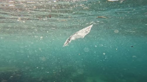 Underwater view of transparent plastic bag floating around in the blue sea.