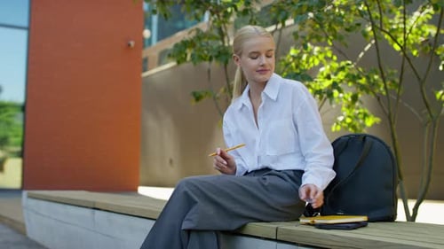 Young Woman Sits on Bench with Notebook Outside