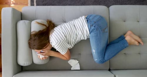 Femme frustrée se couvrant le visage et pleurant allongée seule sur le canapé à la maison