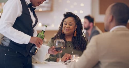 A waiter topping up a couple's wine glasses in a restaurant