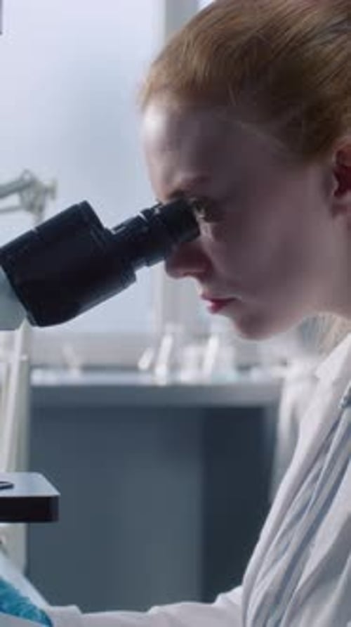 In Modern Medical Laboratory Female Microbiologist Works with Microscope