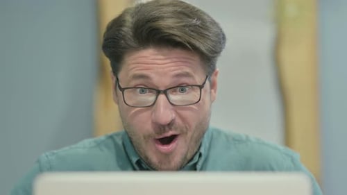 Nahaufnahme eines Mannes mittleren Alters, der Erfolg auf dem Laptop feiert