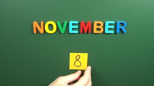 Hand sticking a sticker 8 November calendar day on school board. 8 date of November. Eighth day