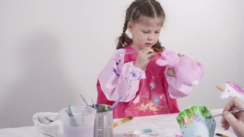 Kleines Mädchen bemalt Pappmaché-Figuren mit Acrylfarbe für ihr Homeschooling-Kunstprojekt