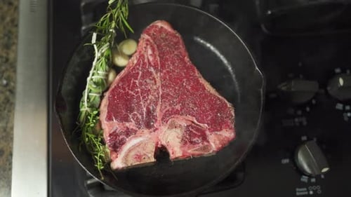 Slo-mo footage moving over a juicy steak, garnished in herbs and spices, slowly cooking in a cast ir