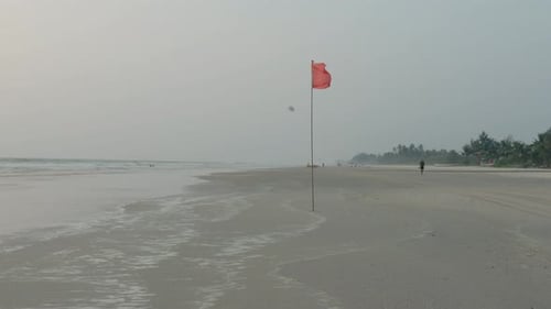 Person Walking on Beach with Red Flag Waving