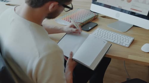 Office Worker Analyzing Diagrams and Taking Notes at Desk