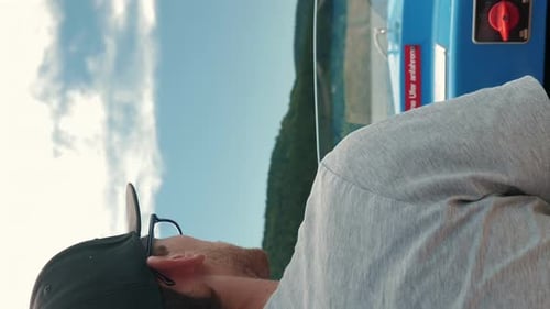 Man driving electric boat along lake surrounded by green trees. Vertical video