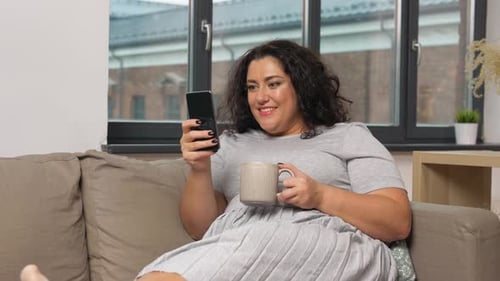 Woman Relaxes on Couch with Phone and Coffee