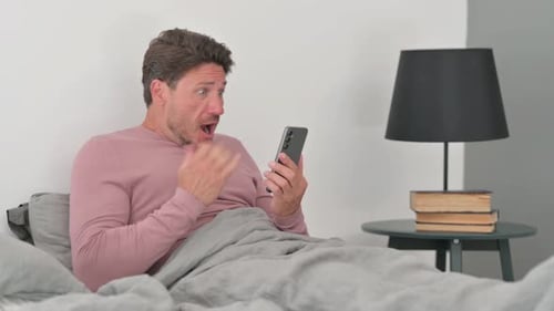 Middle Aged Man Upset by Loss on Phone in Bed