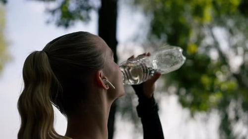 Close-up of an athletic young woman after an active morning jog and workout drinks water