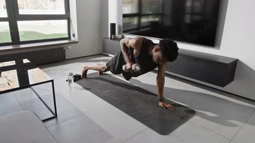 African American Gen Z Man Doing Renegade Row in Plank Position on Exercise Mat