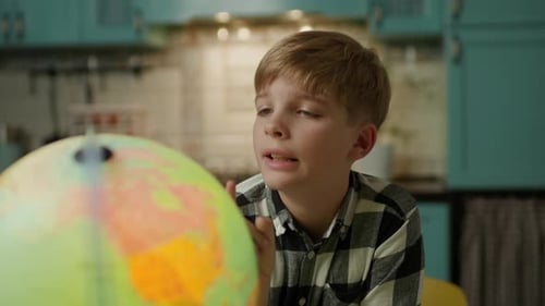 Blond Boy Contemplates Globe in a Cozy Kitchen
