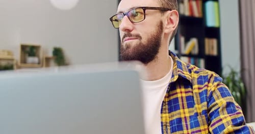 Close Up of Caucasian Man in Glasses and with Beard Sitting at Laptop Computer and Looking with