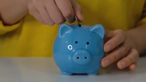 Piggy Bank Business Concept A Hand is Putting a Coin in a Piggy Bank on a Blue Background Saving