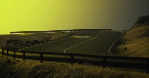 Scenic Winding Road Through Grassy Hills with a Golden Sky at Sunset