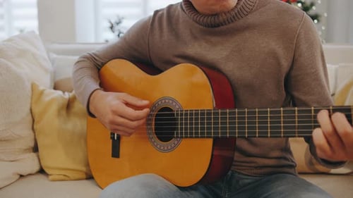 Man Plays Acoustic Guitar on Sofa at Home