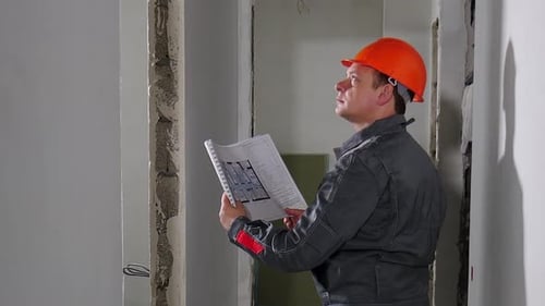 Männlicher Vorarbeiter prüft Verbesserungen im Rahmen eines Renovierungsprojekts in der Wohnung, die Master Man Wearing trägt