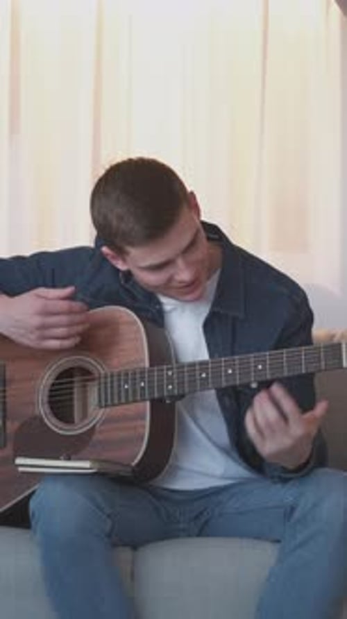Man Plays Acoustic Guitar Sitting on Couch