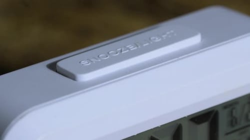 Finger pushes snooze button on an alarm clock