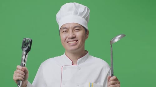 Close Up Of Asian Man Chef Smiling And Showing Tongs And Ladle To Camera In The Green Screen