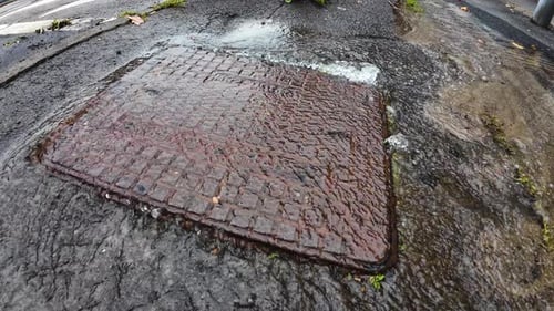 Burst Drain Cover with Treated Water Pouring Out into Street. Leaking Liquid in Need of Repair.