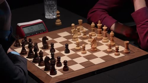 Chess opening moves on wooden board with two opponents and tournament clock running in the backgroun