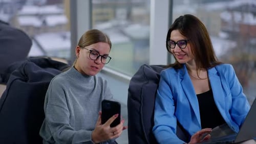 Two Women Collaborating on a Laptop and Smartphone