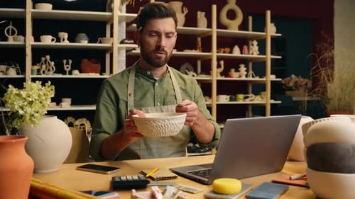 Man Designs Pottery at Laptop in Studio