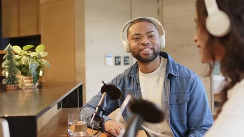 Female host starting discussion, male host wearing headphones, nodding at counter with microphones