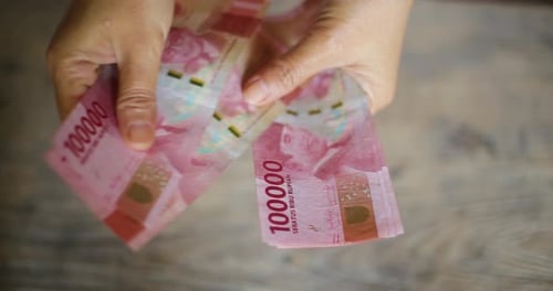 Hands Counting Indonesian Rupiah Banknotes on Wooden Table