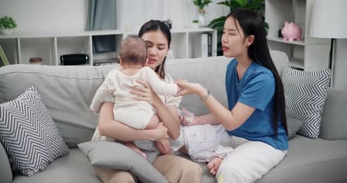 Two Young Women Play With Infant on Couch
