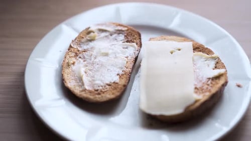 Person putting cheese on toasted bread covered with butter.