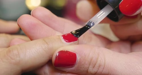In a beauty center, a woman gets her manicure done. At the end of treatment a red enamel is applie