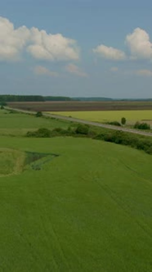 Aerial view of rural road through green fields and farmland under cloudy sky