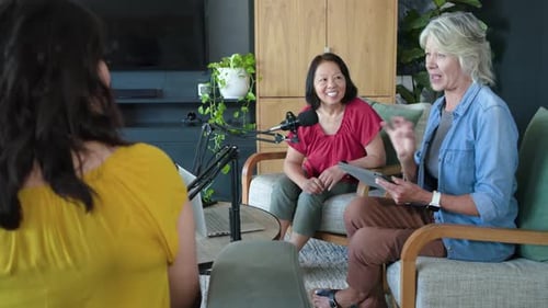 Hôtes féminines matures se penchant vers le micro, parlant et répondant aux instructions de la tablette dans le salon