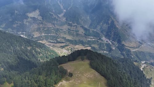 Aerial drone shot of a valley captured from the peak of a mountain covered in the clouds.