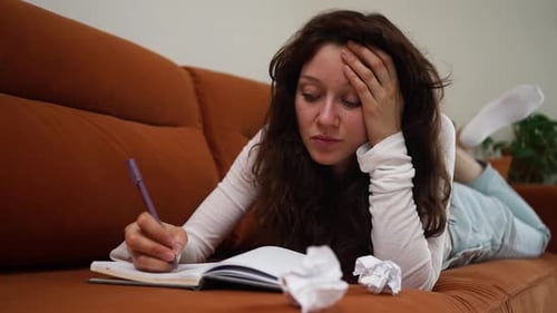 Frustrated Woman Writing, Lying on Couch with Crumpled Paper