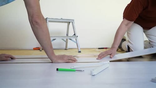 Adults Installing Laminate Wood Flooring in a Home