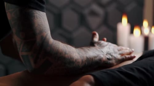 Tattooed Arm Massaging Person's Leg With Candles