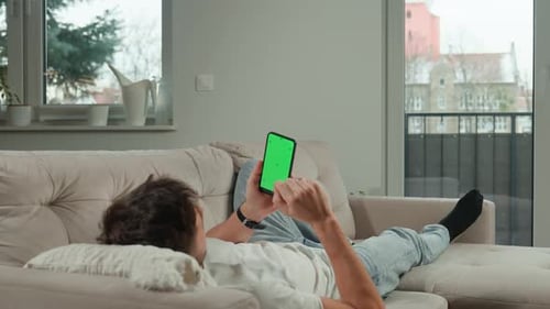 Man Relaxing on Sofa Using Smartphone with Green Screen