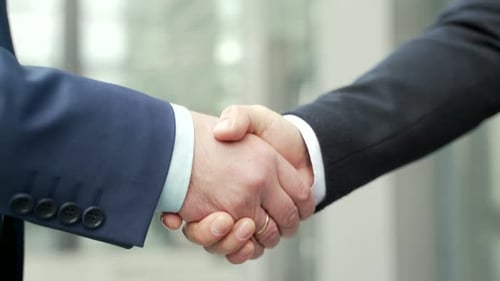 Close up business people shaking hands partnership deal while standing outside on the street near